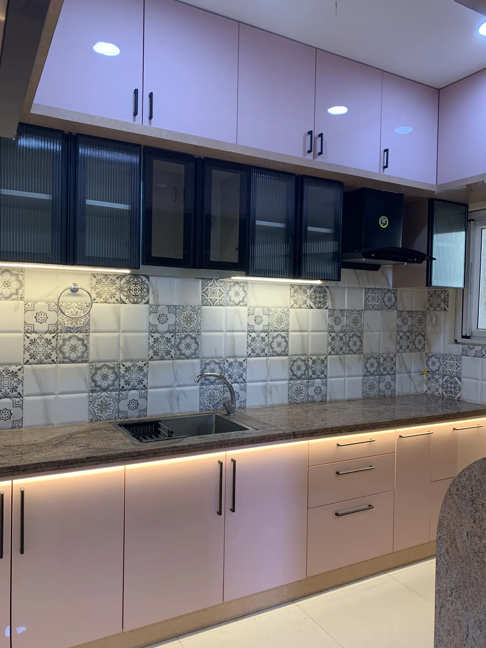 Pink and dark glass kitchen with patterned tile and under-cabinet light
